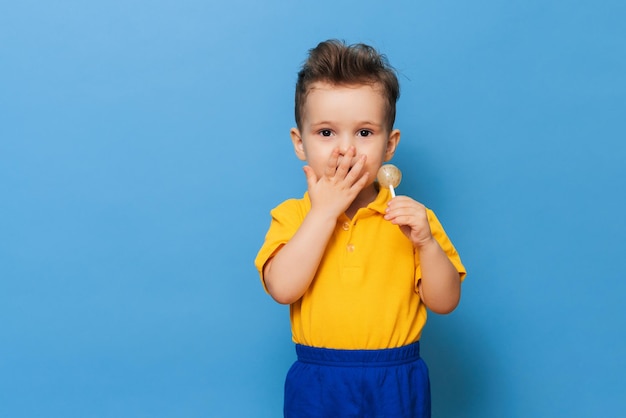 A charming boy looks at the camera while holding a lollipop on a blue background Prevention of childhood caries