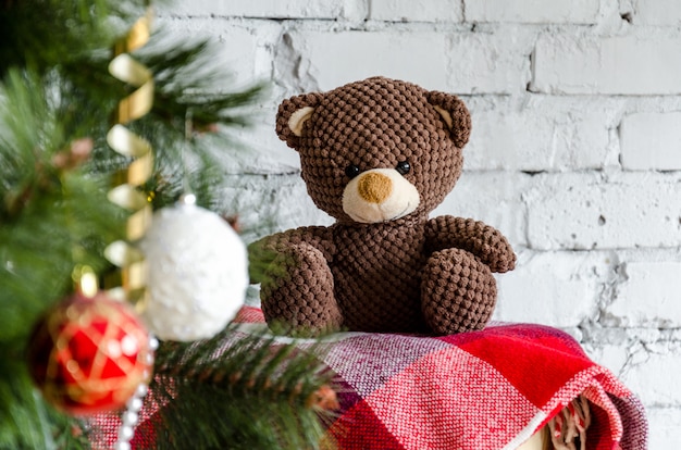 charming brown Teddy bear sitting on a red blanket near the Christmas tree