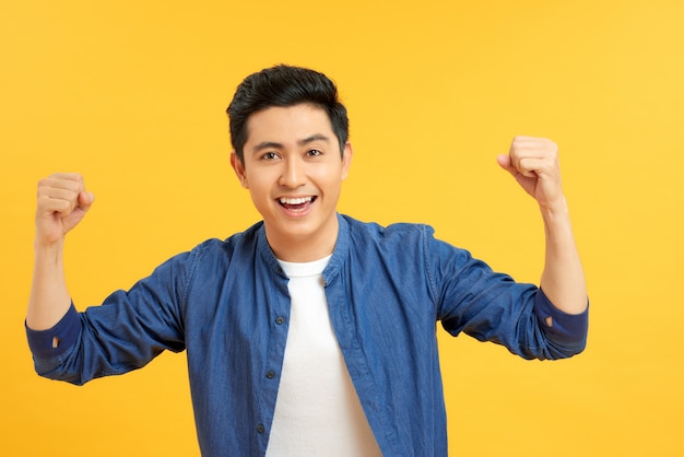 Charming casual man with hands up in the air while looking up victorious on yellow studio background