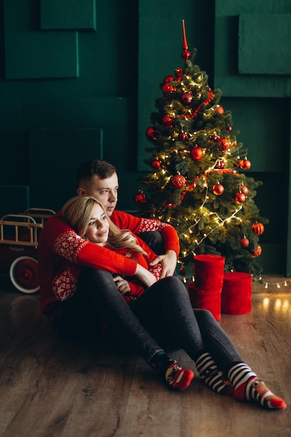 A charming couple in love in traditional Christmas red sweaters spend time near the Christmas tree