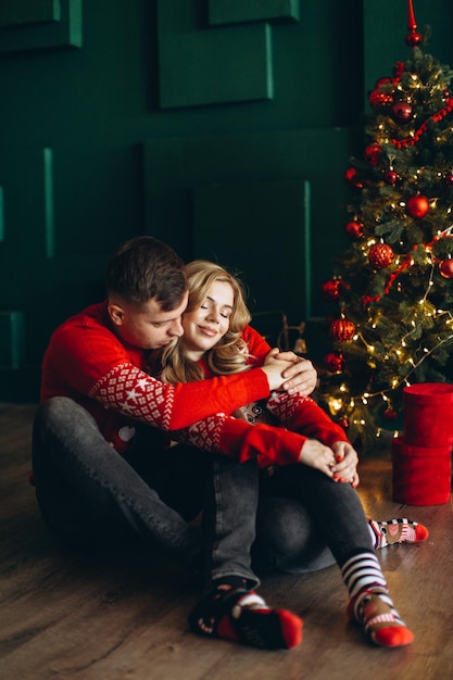 A charming couple in love in traditional Christmas red sweaters spend time near the Christmas tree