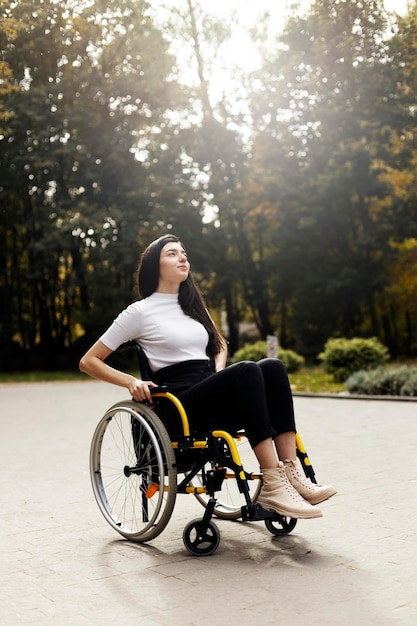 Charming disabled woman sits in a wheelchair Attractive girl raised her head looking up outdoors