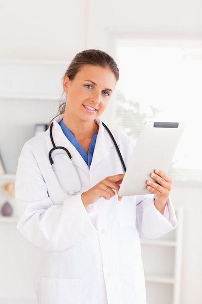 Charming doctor having a stethoscope around her neck pointing at a file looking at the camera