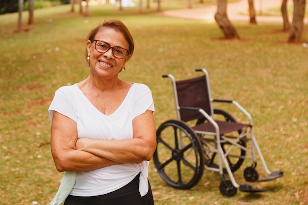 Charming elderly woman smiling in the park standing with the wheelchair in the