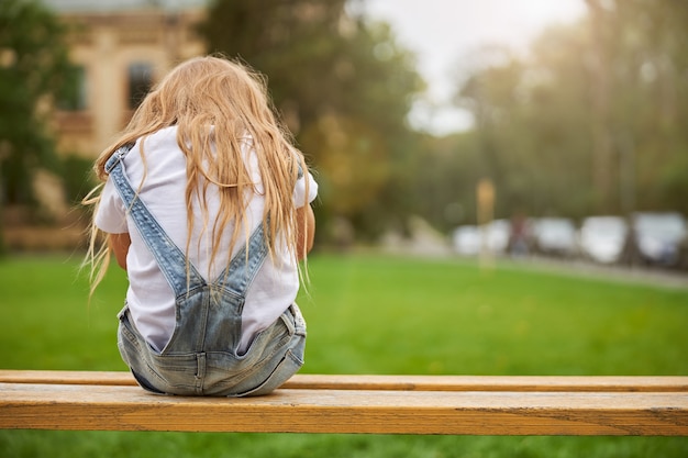 charming female child sitting on the wooden bench in the city park