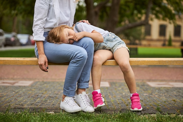 charming female sitting on the wooden bench while resting with her daughter