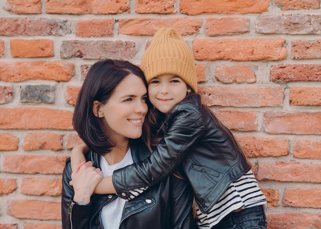 Charming friendly little child and her mother embrace each other dressed in black leather jackets