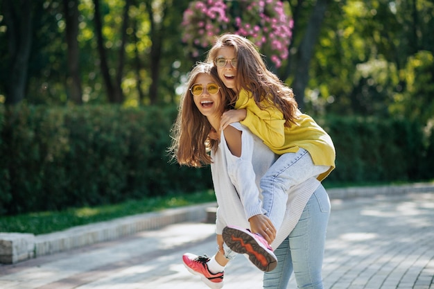 Charming girl in bright sweater around in city Outdoor shot of two young ladies having fun together in sunny warm weekend