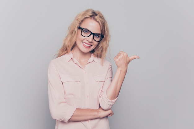 Charming girl in shirt shows her finger on an empty space isolated on gray