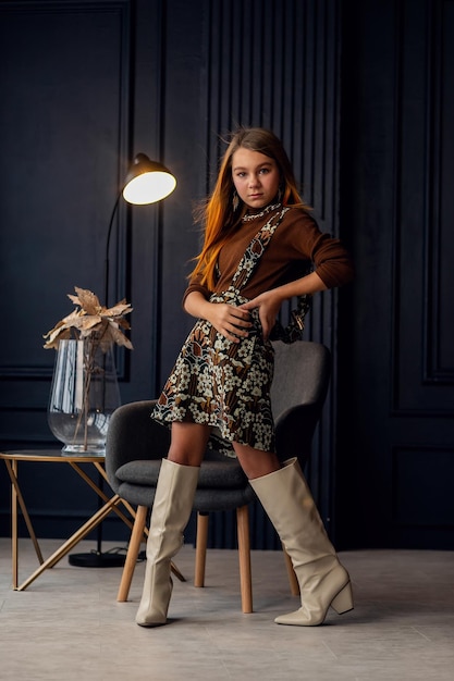 Charming girl with hair in posing in her mothers suede boots Childhood young actress Full length shot isolated interior background Little daughter trying on mothers shoes Imitation of adults