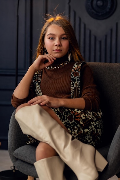 Charming girl with hair in posing in her mothers suede boots Childhood young actress Full length shot isolated interior background Little daughter trying on mothers shoes Imitation of adults