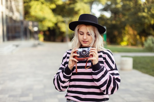 Charming hipster girl in hat with retro camera outdoors