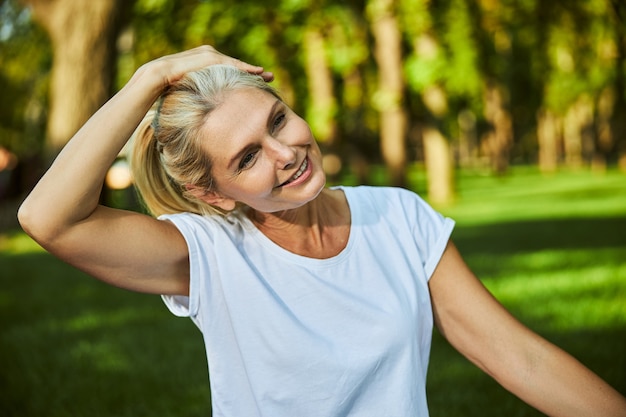 Charming lady looking away and smiling while placing hand on her head