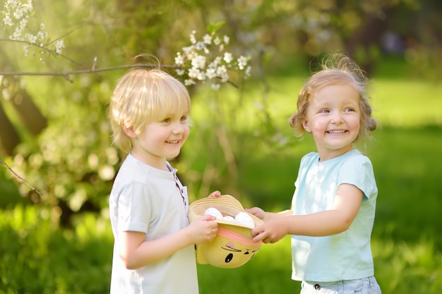 Charming little children hunts for painted eggs in spring park on Easter day.