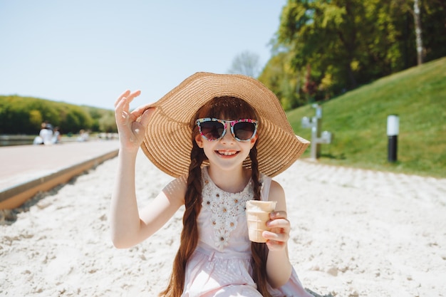 Charming little girl in a hat eats ice cream on the beach of the beach Summer vacation concept