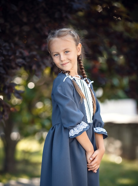 Charming little girl in a retro dress walking in the city on a sunny summer day. Little girl wear school uniform. Primary school girl with long hair. Study and education.