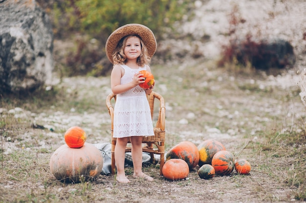 charming little girl in a straw hat, wicker chair, pumpkins, autumn