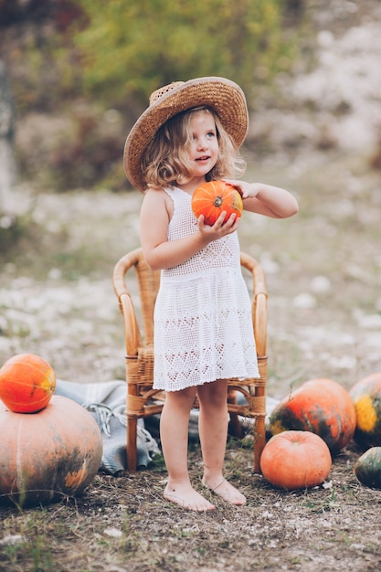 charming little girl in a straw hat, wicker chair, pumpkins, autumn