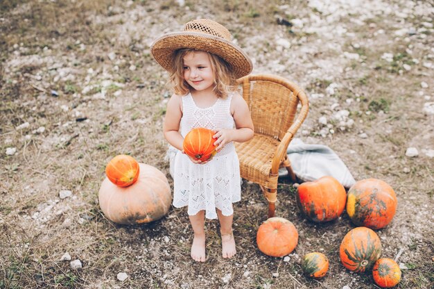 charming little girl in a straw hat, wicker chair, pumpkins, autumn