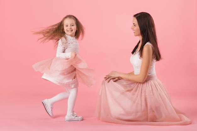 Charming mother and smiling daughter on pink background