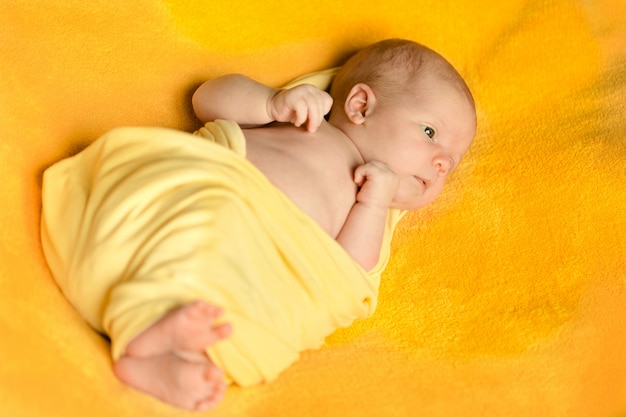 A charming newborn baby lies on a yellow blanket wrapped in a yellow plaid.