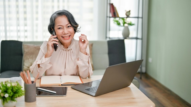 Charming senior asian businesswoman talking on the phone with her business supplier