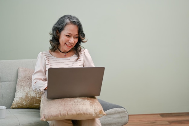 Charming senior asian woman watching something interesting on the internet on her laptop