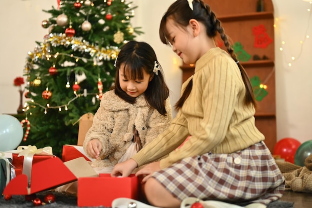 Charming siblings sitting on floor in decorated living room opening Christmas gift Holidays