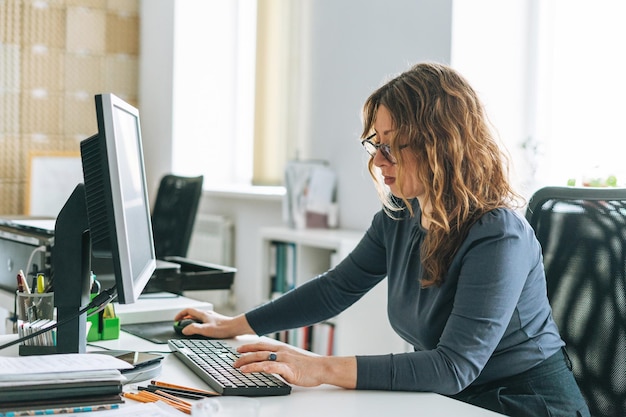 Photo charming smiling adult woman middle aged woman with curly hair architect designer on computer