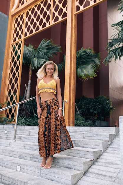 Charming smiling beauty in a bright yellow top and a long skirt posing on the steps.