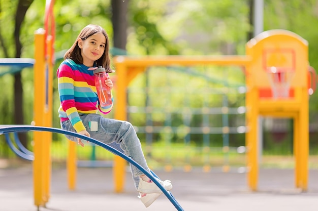 Charming smiling little girl sitting with a plastic bottle of water on the playground