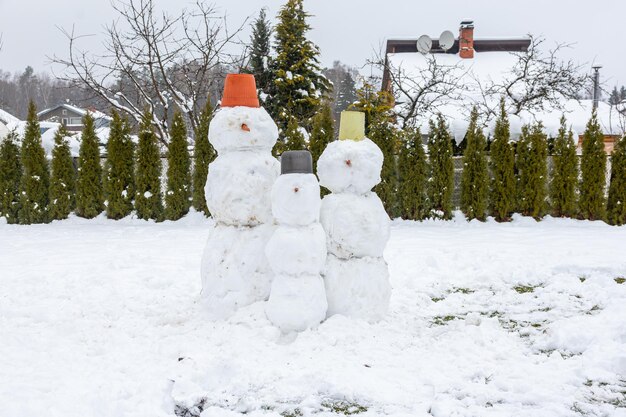 Photo charming snowmen family created in winter yard with festive bucket hats surrounded by snowy trees and a cozy house