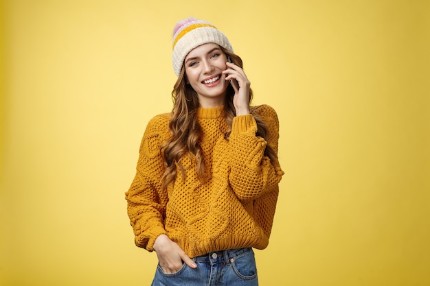 Charming stylish european woman wearing hat sweater tilting head flirty smiling talking smartphone c...