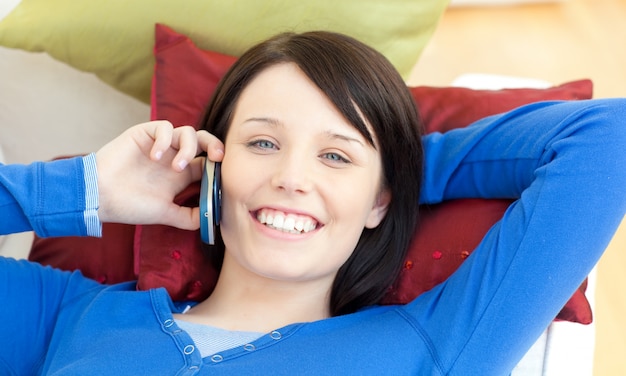 Charming teen girl talking on phone lying on a sofa 