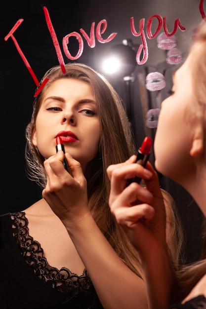 Charming woman applying red lipstick and looking in mirror