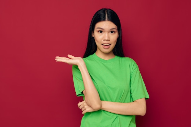 Charming young Asian woman green tshirt gestures with his hands red background unaltered