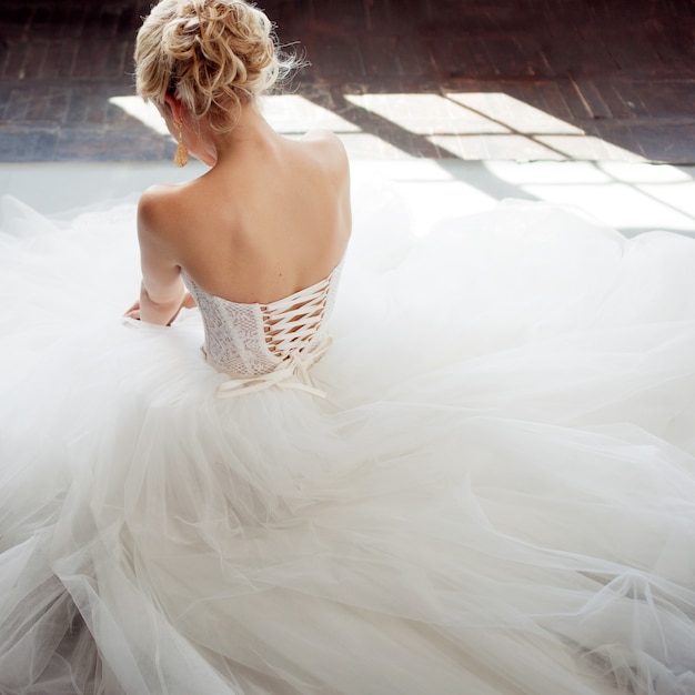 Charming young bride in luxurious wedding dress. Pretty girl in white. Gray background. Back