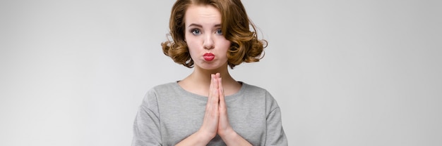 Charming young girl in a gray T-shirt on a gray background. The girl folded her hands together