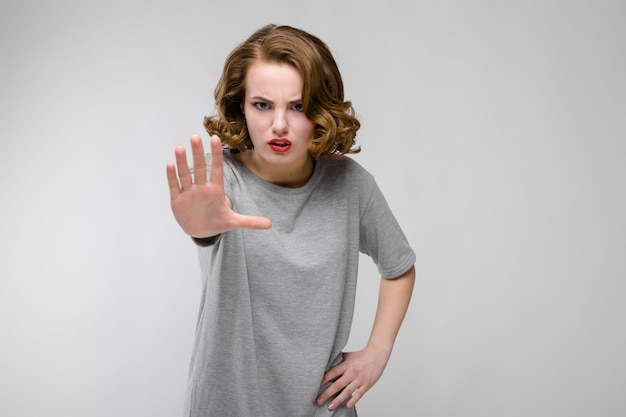 Charming young girl in a gray T-shirt on a gray background. The girl held out her hand.