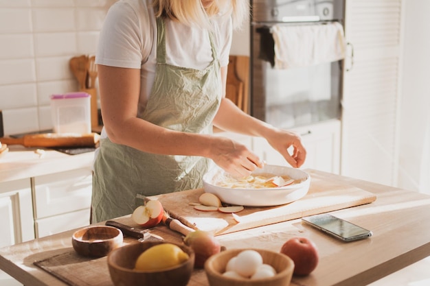 Charming young woman in chef's apron preparing pie at home in the kitchen Cozy home interior