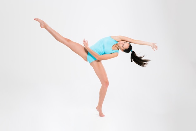 Charming young woman doing acrobatic stunt isolated on a white wall