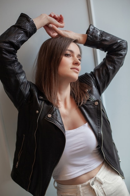 Charming young woman posing in black leather jacket and white jeans on a white background. Beauty, fashion.