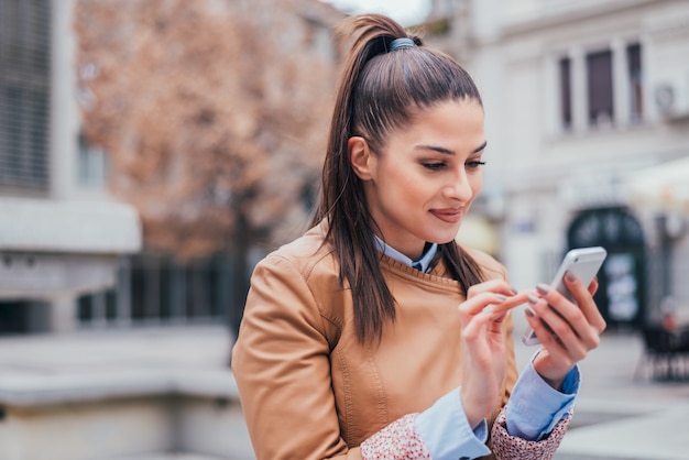 Charming young woman using smartphone outdoors. Close-up.