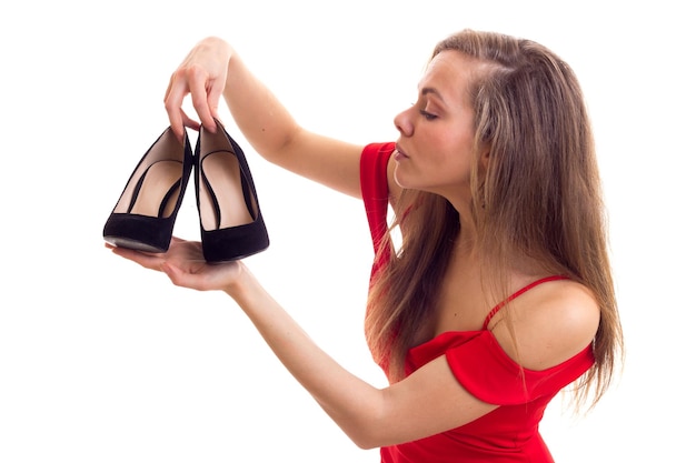 Charming young woman with long brown hair in skimpy red dress holding a pair of black stiletto shoes