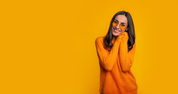 Charming young woman in yellow sweater and sunglasses while she posing with smile on yellow background and looking on camera