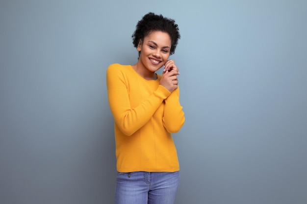 Charming young year old hispanic lady with an afro tail is dressed in a casual bright yellow sweater