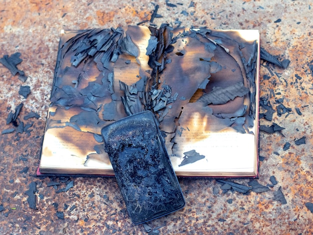 Charred phone and book on a metal surface after a fire