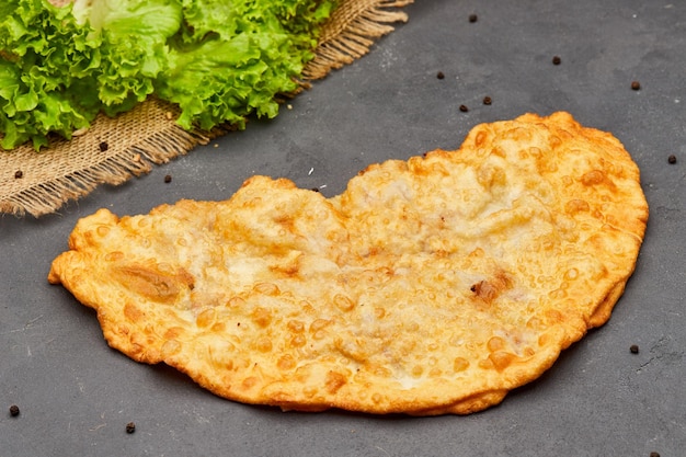 Cheburek fried pie with meat and onions on dark stone background Unhealthy food Traditional dish of many turkic and mongolian peoples