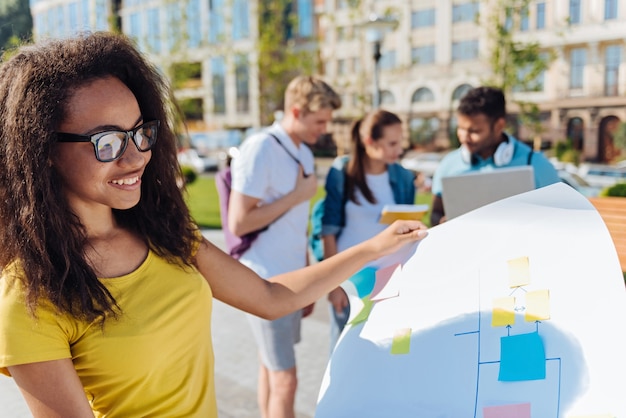 Check it all. Beautiful clever brunette female expressing positivity while holding her project and standing on the foreground