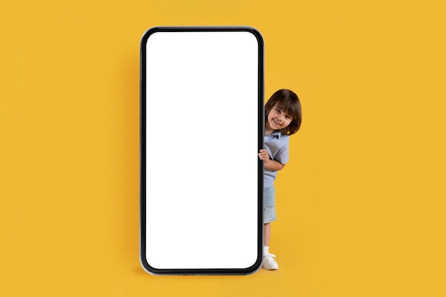 Check this app Adorable little boy looking out of big smartphone with blank screen and smiling yellow background